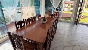 A dining area with a wooden table and chairs, a ceiling fan, and large windows with a view of the outdoors. - QUINTA ANUBIS (Oaxtepec)