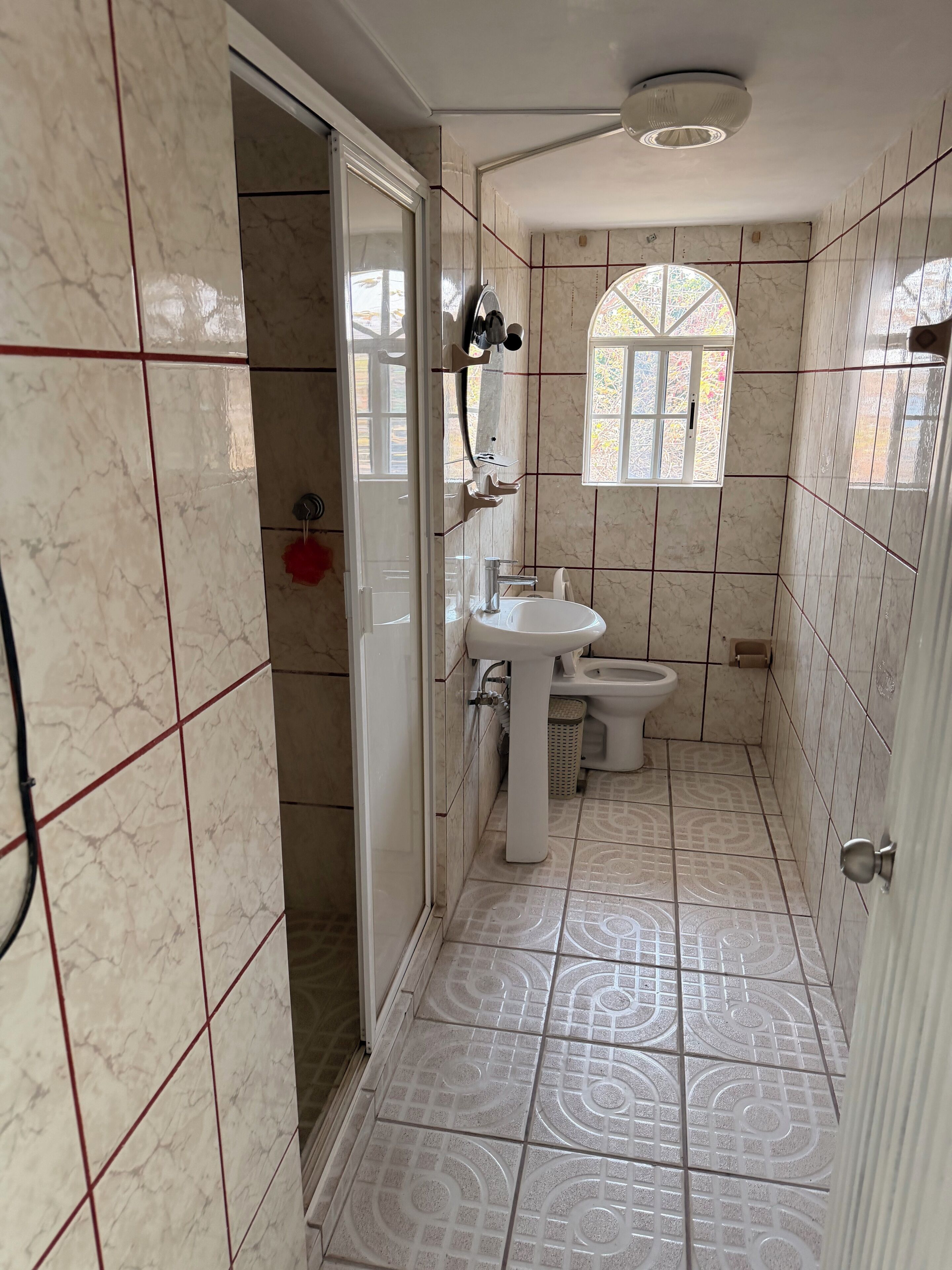 A bathroom with a toilet, sink, and shower area, featuring marble tiles and a window.