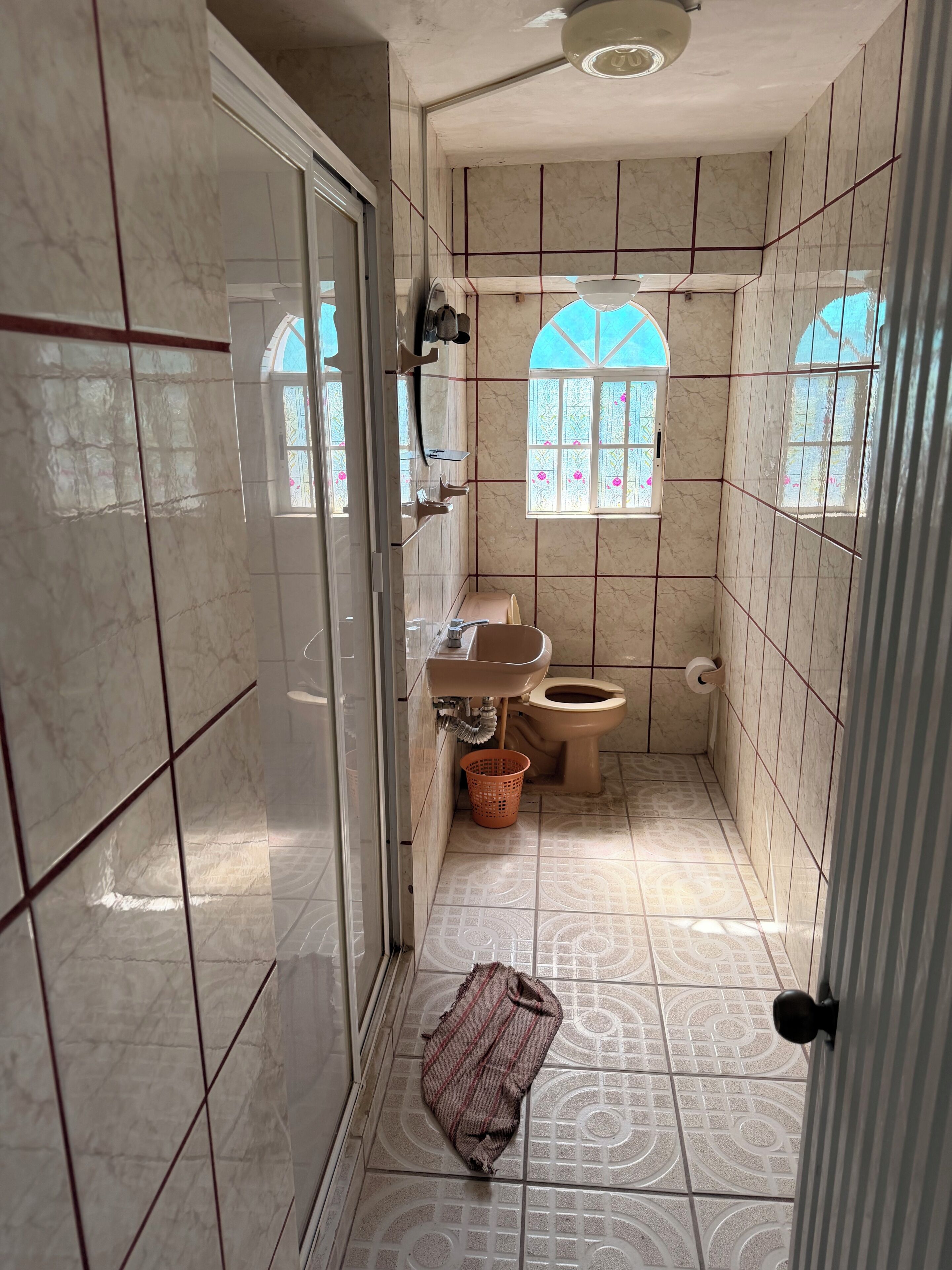Une salle de bain avec douche, toilettes et lavabo, des murs carrelés et une fenêtre donnant sur un paysage agréable.