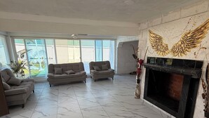 A spacious living room with a fireplace, large windows, and a view of the backyard. - QUINTA ANUBIS (Oaxtepec)