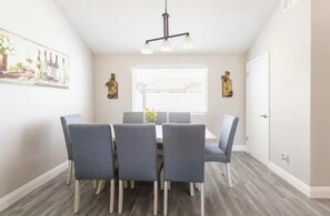 A dining area with a table and chairs, a window with blinds, and a painting on the wall. - Modern 4 BR Home w/ Pool-Sleeps 10-Near Strip (Las Vegas)