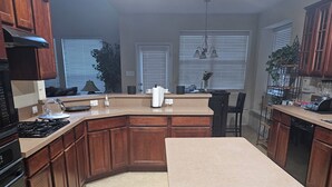 A kitchen with wooden cabinets, a central island, a stove, and a dining area with a chair. - Fresh Baked Cookies /Brownies with  check in from Sweet Vegan Cookie Company (Mesquite)