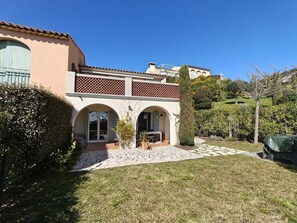 Ein Haus mit einer Terrasse, einem überdachten Sitzbereich im Freien und einem Garten mit verschiedenen Pflanzen.