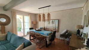 Ein Wohnzimmer mit einer Couch, einem Esstisch mit Stühlen, einem Couchtisch und einem Bild von einer Strandlandschaft.