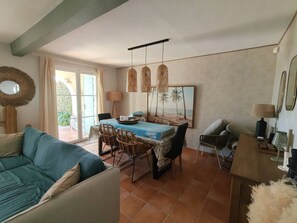 Ein Wohnzimmer mit einer Couch, einem Esstisch mit Stühlen, einem Couchtisch und einem Bild von einer Strandlandschaft.