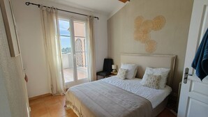 Ein Schlafzimmer mit einem Bett, einem Nachttisch, einem Sessel, einem Fenster mit Vorhängen und einer Wanddekoration.