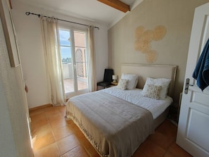 Ein Schlafzimmer mit einem Bett, einem Nachttisch, einem Sessel, einem Fenster mit Vorhängen und einer Wanddekoration.