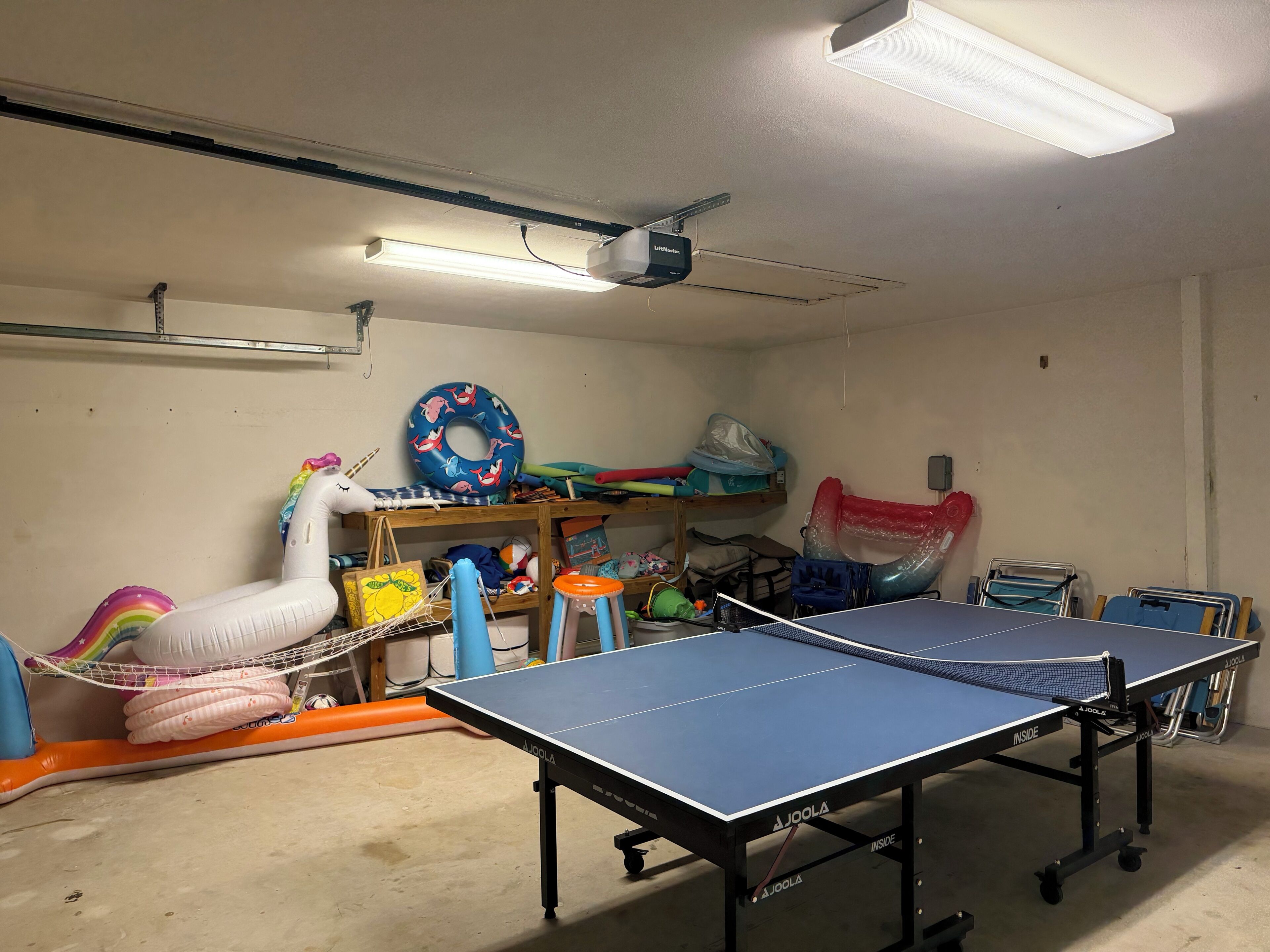 Una habitación con mesa de ping pong, ventilador de techo y varios juguetes y equipo para niños.