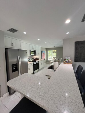 A modern kitchen with a central island, stainless steel appliances, and a view of the outdoors. - Prime Marco Island! 5 Min Walk to Beach • Pool • Family & Pets • JW Marriott (Marco Island)