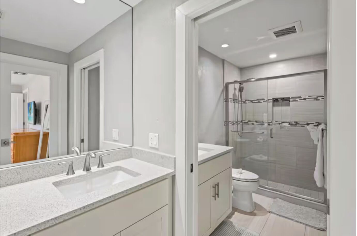 A modern bathroom with a large mirror, two sinks, a toilet, and a glass-enclosed shower.