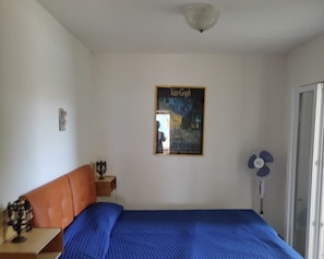 A bedroom with a bed, a nightstand, a wall-mounted picture of Van Gogh, a ceiling light, and a fan.