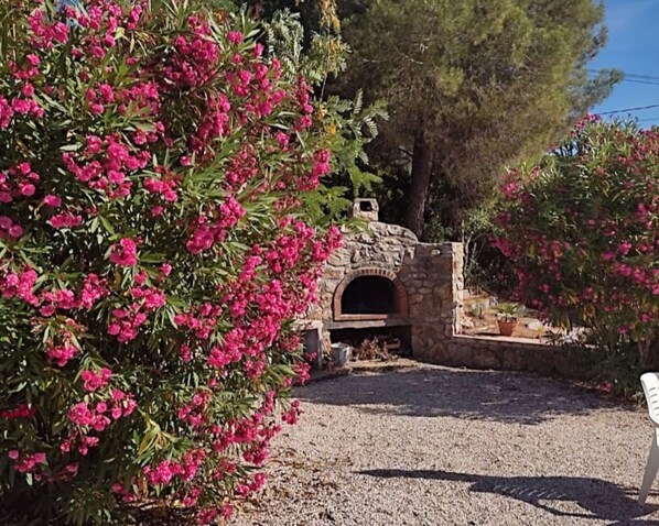 A stone oven structure in a garden with pink flowering plants and trees.