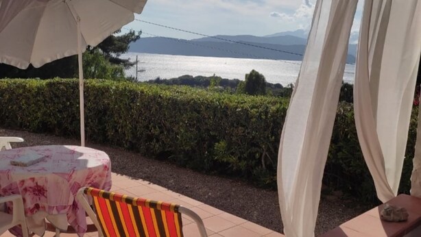 Une terrasse avec une table, des chaises et un parasol, d’où l’on peut admirer un plan d’eau avec des montagnes à l’horizon.