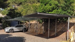 Un abri-voiture fermé avec une voiture garée à l’intérieur, un mur de pierre et des arbres en arrière-plan.