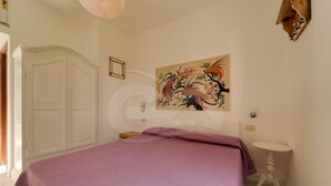 A bedroom with a bed, a white wardrobe, a round mirror, a painting, and a small bedside table. - Aurora Celeste - Goelba (Campo nell'Elba)