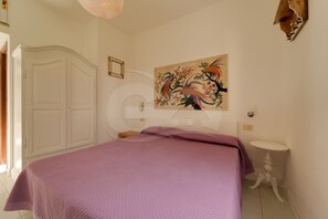 A bedroom with a bed, a white wardrobe, a round mirror, a painting, and a small bedside table. - Aurora Celeste - Goelba (Campo nell'Elba)