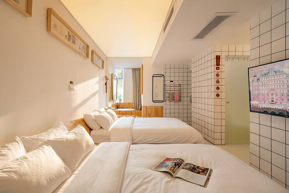 Une chambre d’hôtel avec deux lits, une salle de bain avec un miroir et un téléviseur fixé au mur.