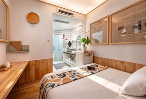 A hotel room with a bed, a desk, a clock, a potted plant, and a bathroom visible through an open door. - T.G.S. Museum Hotel (Guangzhou)