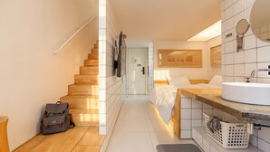 Ein Hotelzimmer mit einer Holztreppe, einem Bett mit weißer Bettwäsche, einem Badezimmer mit Waschbecken und Spiegel sowie einer kleinen Schreibtischzeile.