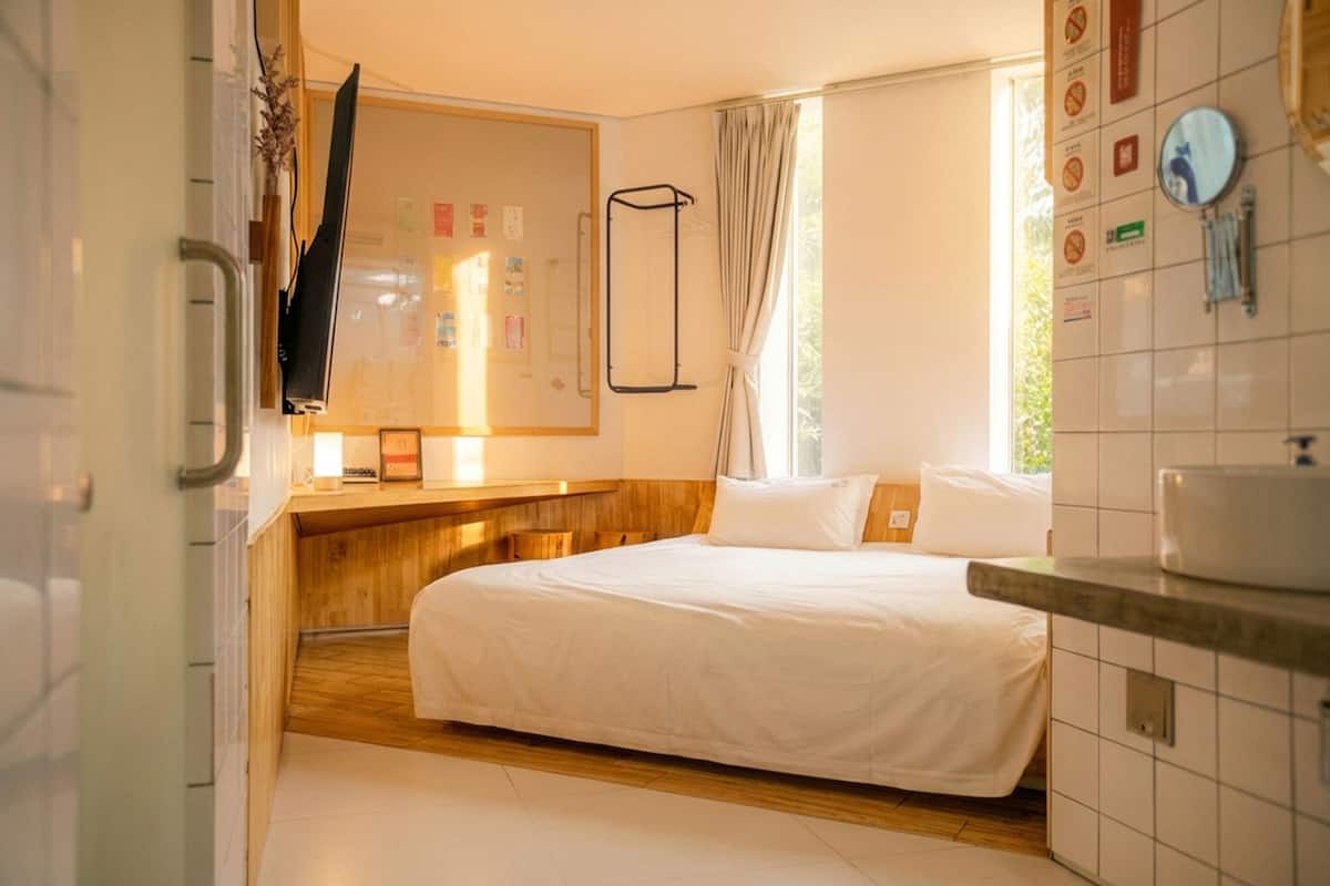 Une chambre d’hôtel avec un lit, des meubles en bois, une fenêtre avec des rideaux, un miroir et un mur orné de panneaux.