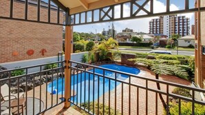 Een balkon met uitzicht op een zwembad, een bakstenen muur en een heldere lucht.