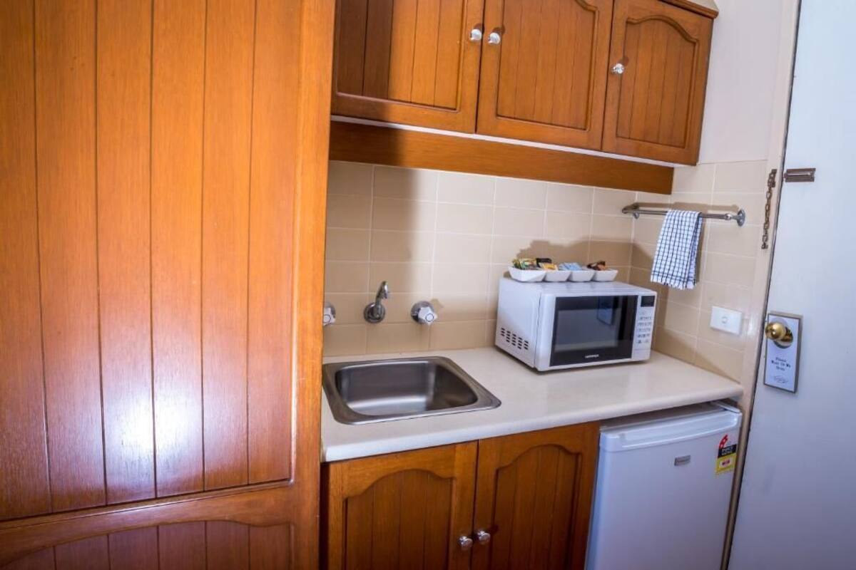Une cuisine compacte avec des meubles en bois, un évier en acier inoxydable, un micro-ondes blanc et un petit réfrigérateur.