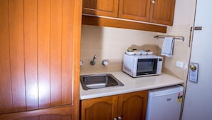 Een compacte keuken met houten kastjes, een roestvrijstalen spoelbak, een witte magnetron en een kleine koelkast.