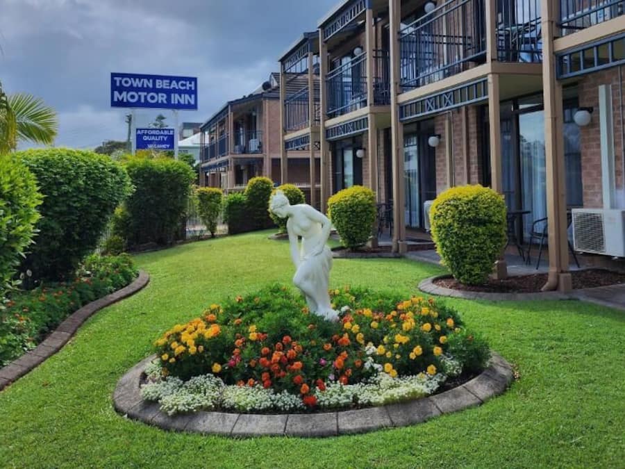 A motor inn with a landscaped garden featuring a statue, a signboard, and a multi-story building with balconies.