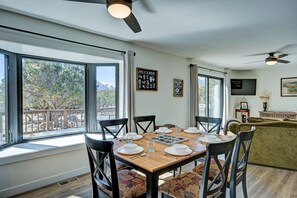 A dining area with a wooden table set for four, surrounded by chairs, with a view of the outdoors through large windows. - Piñon Peak Retreat |Hot Tub |Views |2 Living Areas (Buena Vista)