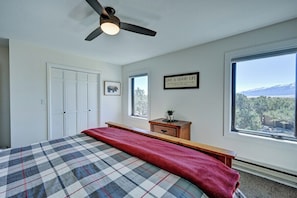 A bedroom with a bed, a ceiling fan, a window with a mountain view, and a wall with a motivational quote. - Piñon Peak Retreat |Hot Tub |Views |2 Living Areas (Buena Vista)
