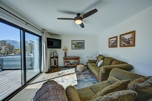 Ein Wohnzimmer mit großem Fenster, Deckenventilator, Sofa, Fernseher und Teppich.