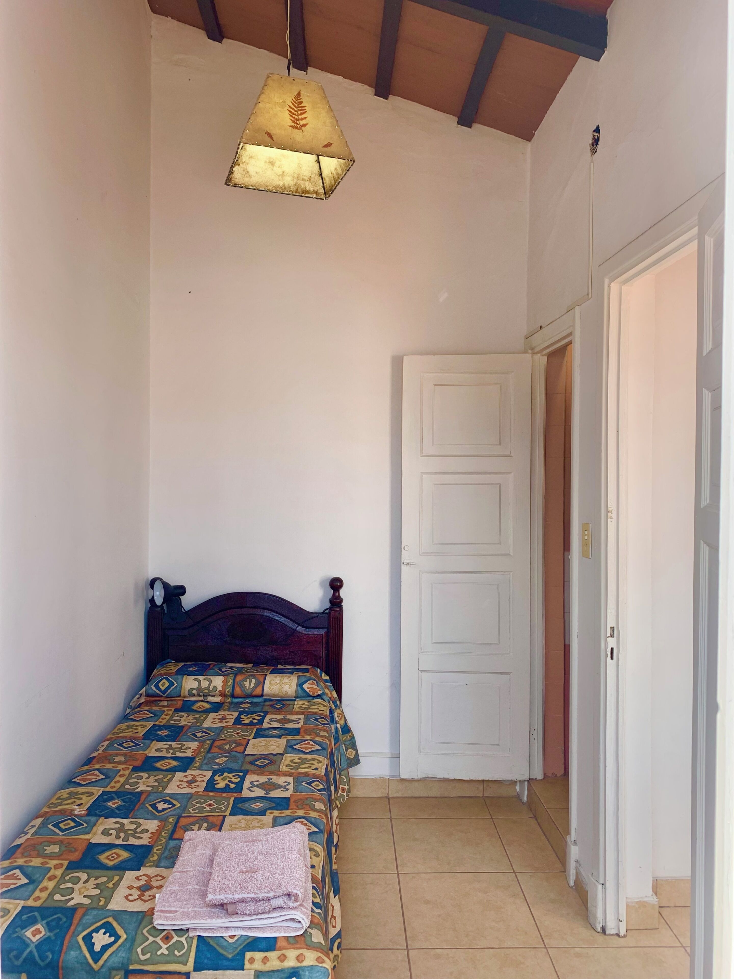 A bedroom with a bed, a hanging light fixture, a white door, and a tiled floor.