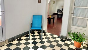A hallway with a checkered floor, a blue chair, a potted plant, and a dining area in the background. - Colonial Apt for 7 · Private Terrace · 3 Bedrooms · 9 Blocks from Main Square (Salta)