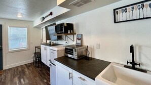 A kitchen with white cabinets, a black countertop, a microwave, a radio, and a framed picture on the wall. - TTStop’s Close to Yellowstone, Fireplace (Island Park)