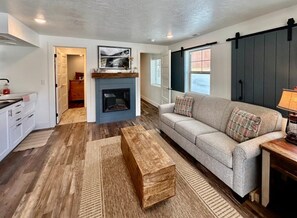 A living room with a sofa, a coffee table, a fireplace, and a sliding door. - TTStop’s Close to Yellowstone, Fireplace (Island Park)