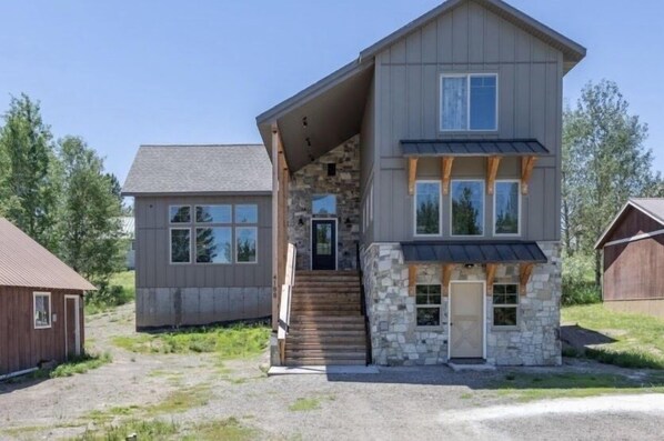 A two-story house with a stone facade, a front porch, and a staircase leading to the entrance. - TTStop’s Close to Yellowstone, Fireplace (Island Park)