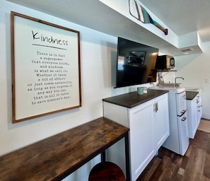 A kitchen with a wooden countertop, white cabinets, a TV, and a framed quote on the wall. - TTStop’s Close to Yellowstone, Fireplace (Island Park)