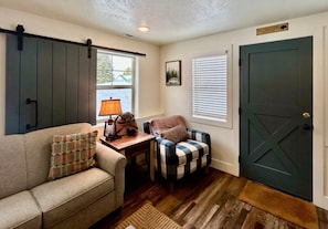 A room with a sofa, a chair, a table, a lamp, a door, and a window. - TTStop’s Close to Yellowstone, Fireplace (Island Park)