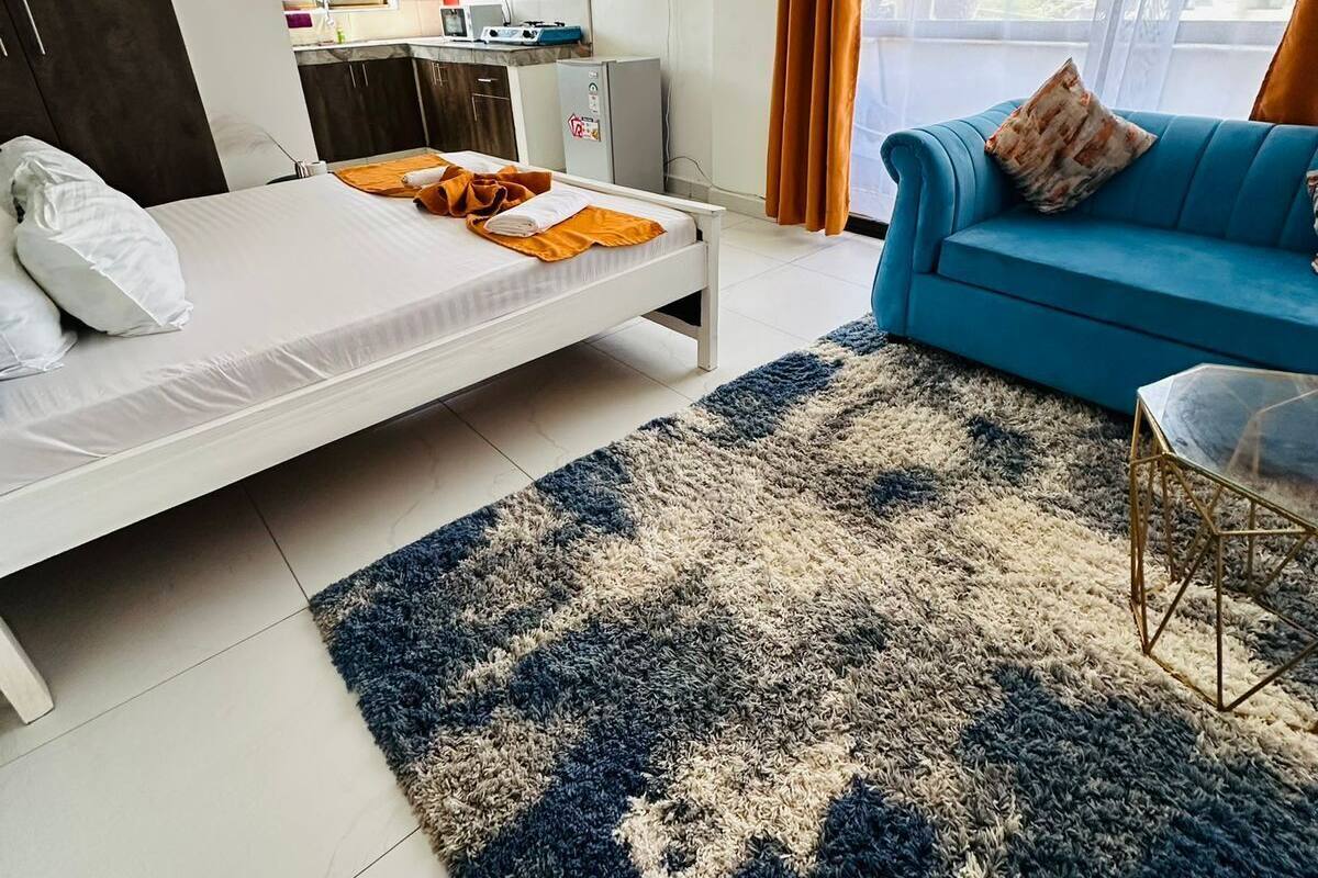 Un dormitorio con cama, un sofá azul, un tapete y una kitchenette al fondo.