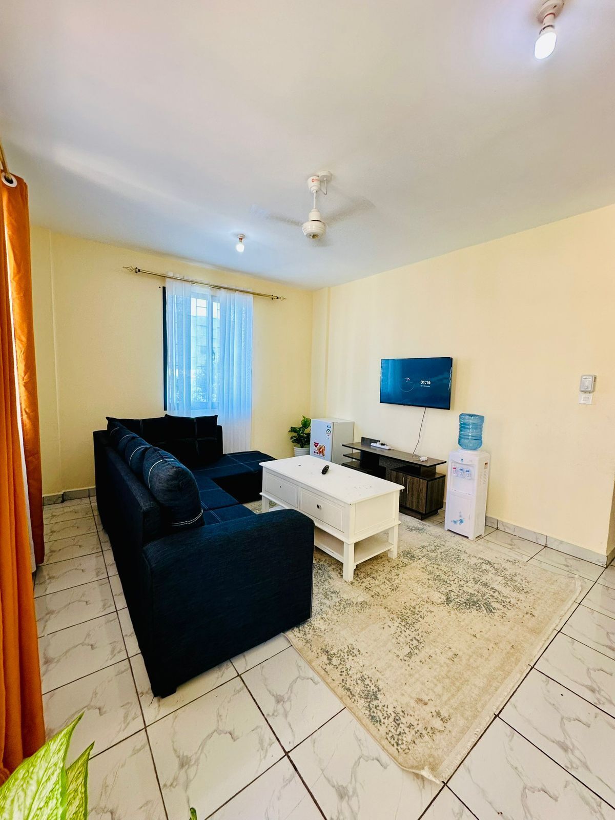 A living room with a sofa, coffee table, TV, water dispenser, and ceiling fan.