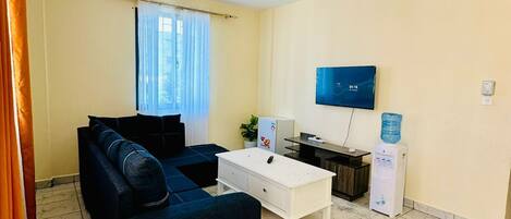 A living room with a sofa, coffee table, TV, water dispenser, and ceiling fan.