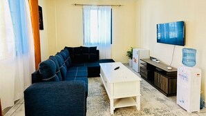 A living room with a sectional sofa, a coffee table, a TV, and a water dispenser. - Zahra Apartments Bamburi (Bamburi)