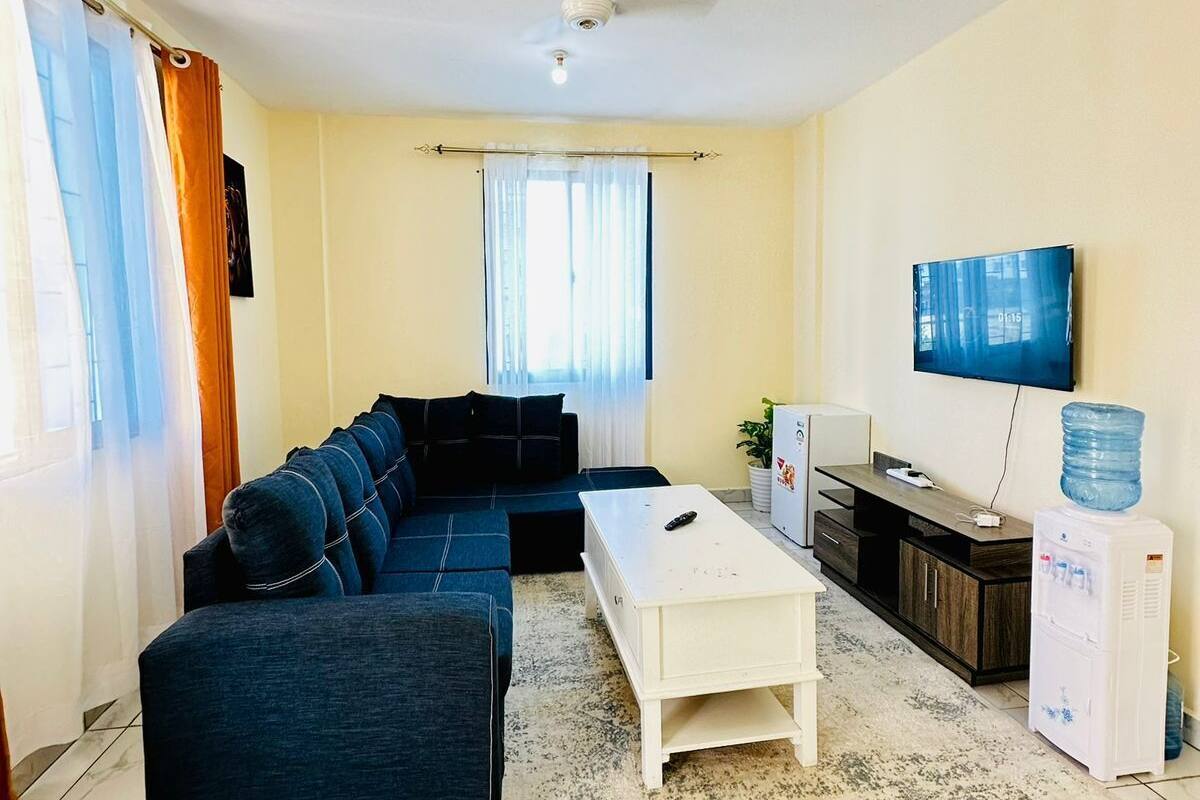 Una sala de estar con un sofá modular, una mesa de centro, un televisor y un dispensador de agua.