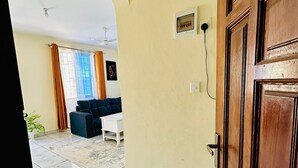 An interior view of a room with a tiled floor, a wooden door, and a living area with a sofa and a TV. - Zahra Apartments Bamburi (Bamburi)