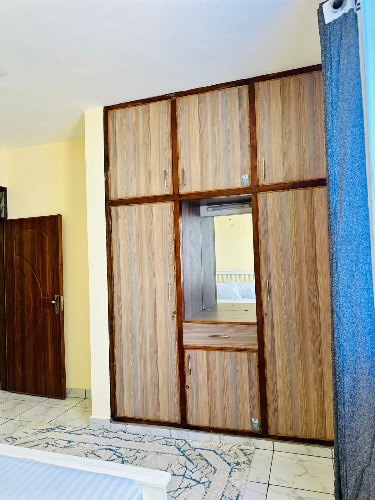 A room with a large wardrobe, a door, and a patterned rug.