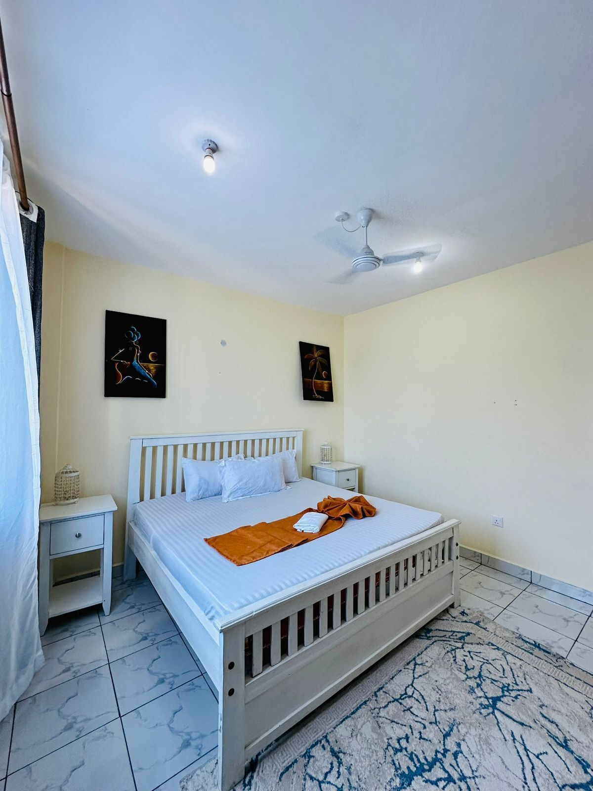 Un dormitorio con cama, mesitas de noche, ventilador de techo y obras de arte en las paredes.