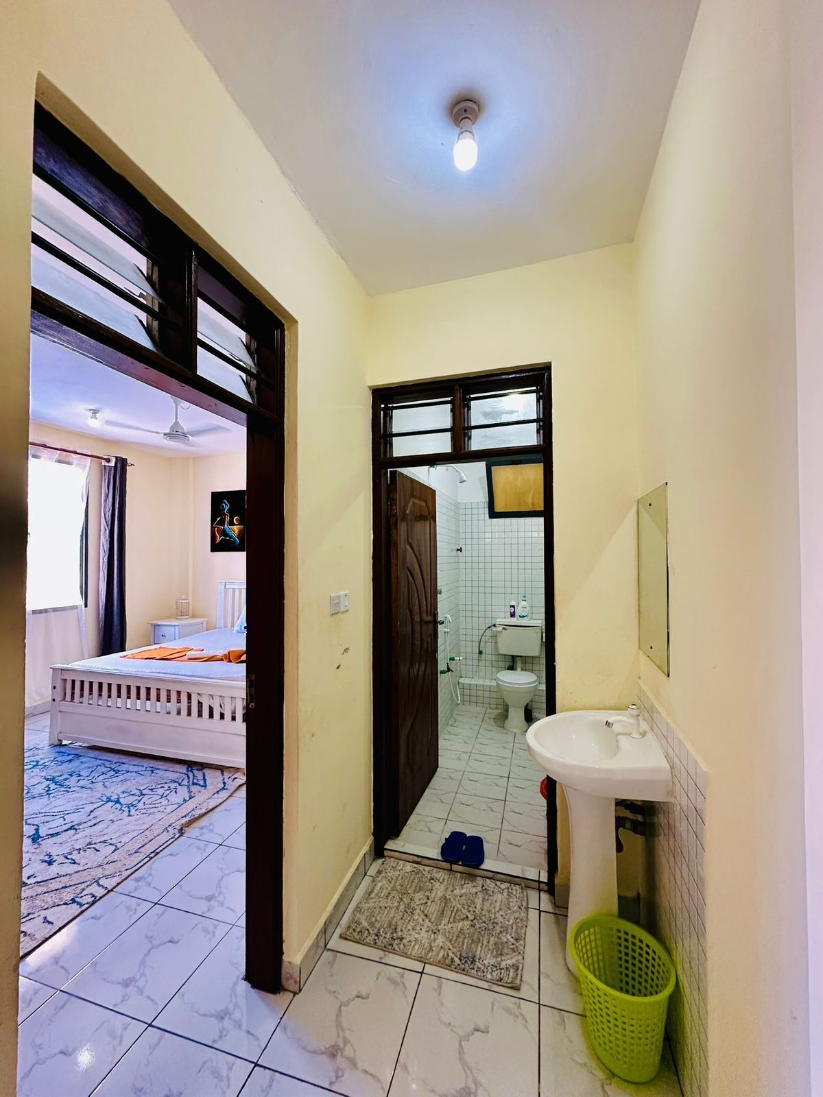 A narrow hallway with a bed, a bathroom, and a sink.