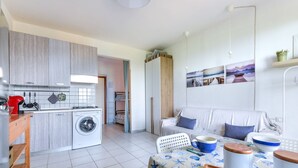 Un espace de vie compact comprenant un coin cuisine, un lave-linge, un coin repas avec une table pour deux personnes et un canapé.