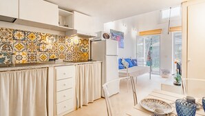 Una cocina compacta con salpicadero de azulejos, un refrigerador blanco y una zona de comedor con mesa y sillas.