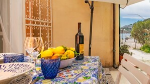 Una mesa con mantel floral, un cuenco de limones, una botella de vino y una copa en un balcón con vistas al mar.